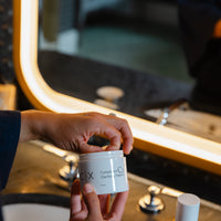 Opening a jar of CMPLXN C2 Clarifying Pads at the bathroom vanity