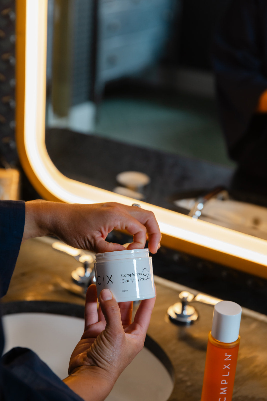 Opening a jar of CMPLXN C2 Clarifying Pads at the bathroom vanity